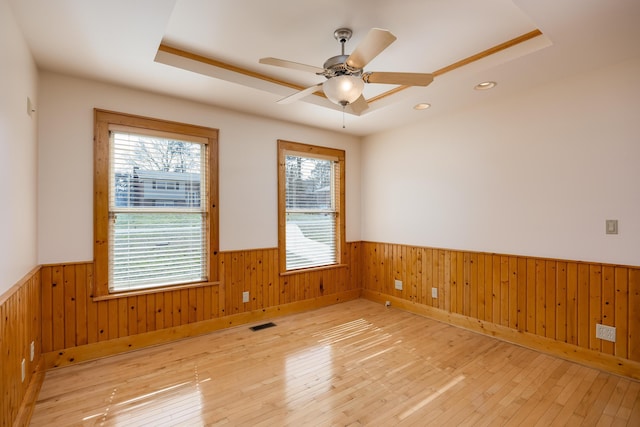 empty room with light wood finished floors, visible vents, a tray ceiling, and wainscoting