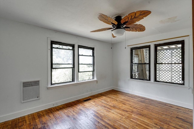 empty room featuring a ceiling fan, wood finished floors, baseboards, visible vents, and heating unit