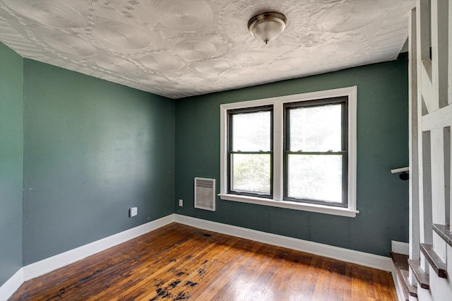 empty room with baseboards, dark wood-type flooring, and heating unit