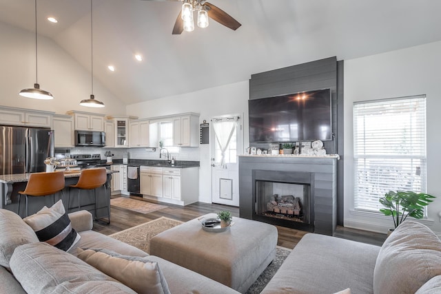 living room featuring high vaulted ceiling, a large fireplace, dark wood finished floors, and a ceiling fan