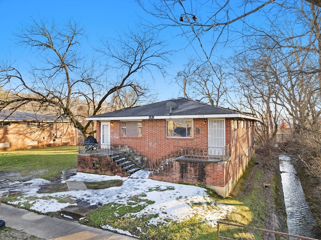 view of snowy exterior featuring brick siding and a lawn