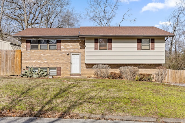 split foyer home featuring brick siding, fence, and a front lawn