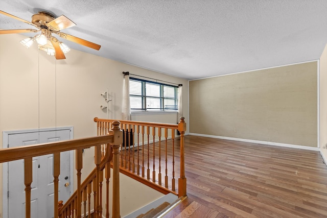 staircase with a textured ceiling, wood finished floors, ceiling fan, and baseboards