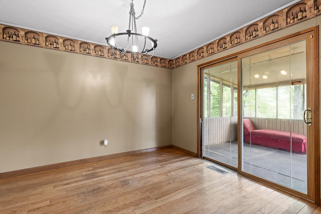 empty room featuring a chandelier, light wood-style flooring, and baseboards