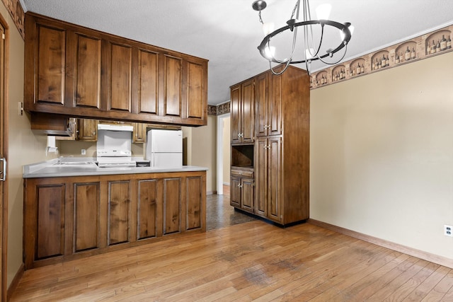 kitchen with freestanding refrigerator, range, a chandelier, a peninsula, and light wood-style floors