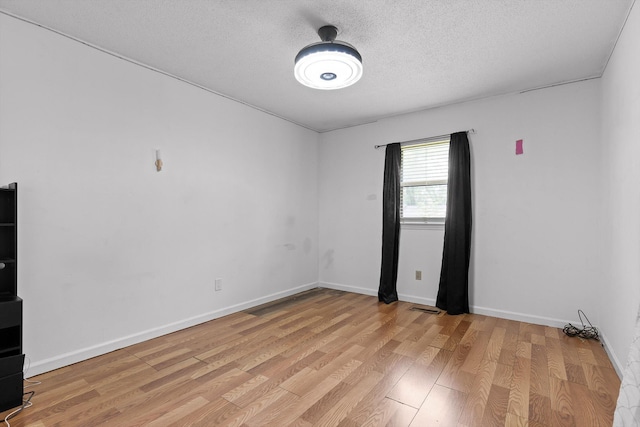 empty room featuring light wood-style floors, baseboards, and a textured ceiling