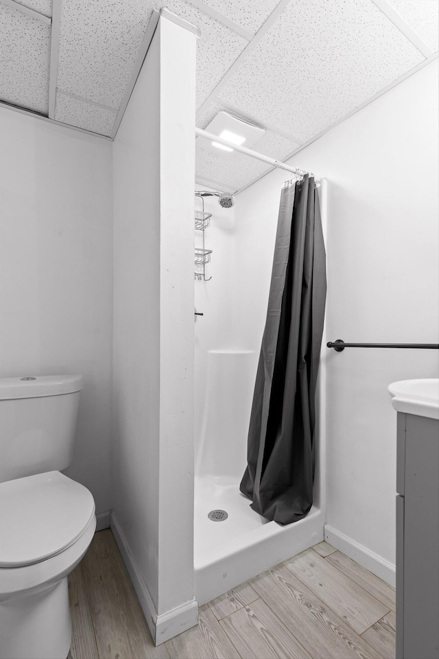 bathroom with a paneled ceiling, a stall shower, toilet, wood finished floors, and baseboards
