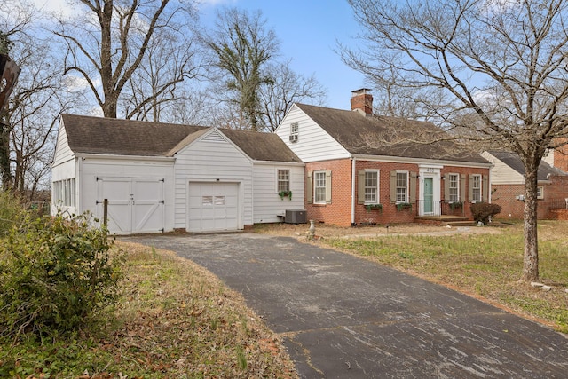 cape cod-style house with driveway, an attached garage, a chimney, central air condition unit, and brick siding