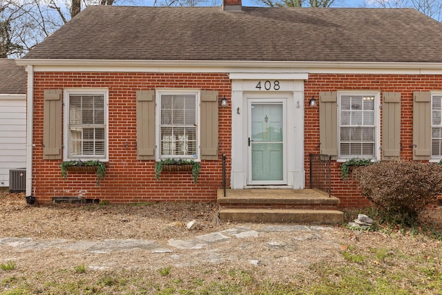 view of front of house with central AC, brick siding, roof with shingles, and a chimney