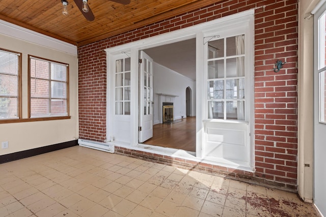 empty room featuring brick wall, baseboards, ceiling fan, wood ceiling, and tile patterned floors