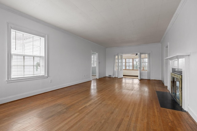 unfurnished living room with a fireplace with flush hearth, plenty of natural light, light wood finished floors, and ornamental molding