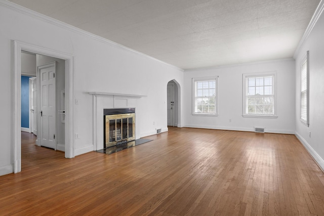 unfurnished living room with hardwood / wood-style floors, visible vents, arched walkways, ornamental molding, and a tiled fireplace