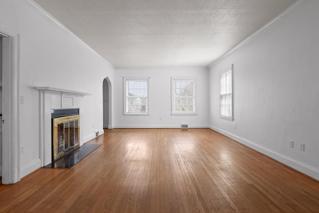 unfurnished living room featuring wood-type flooring, a healthy amount of sunlight, crown molding, and a tile fireplace