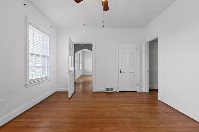 unfurnished room with visible vents, a ceiling fan, wood finished floors, arched walkways, and crown molding