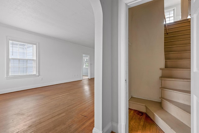 staircase featuring a wealth of natural light, ornamental molding, baseboards, and wood finished floors