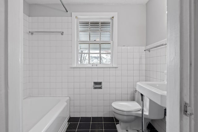 bathroom with tile patterned floors, toilet, tile walls, and a wainscoted wall