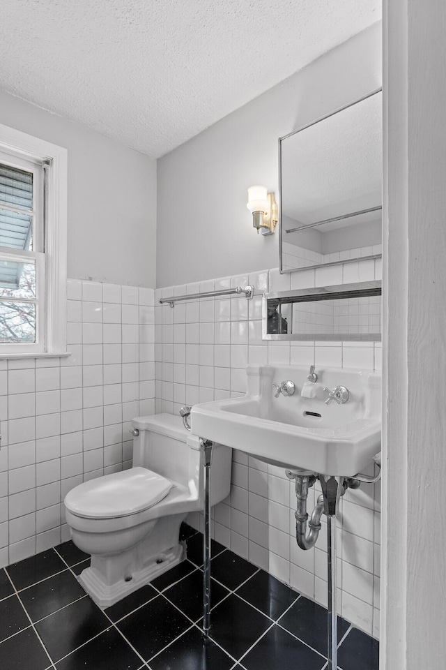 half bathroom featuring tile patterned floors, toilet, a textured ceiling, and tile walls