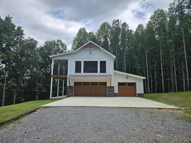 view of front of home with driveway, a garage, a view of trees, stone siding, and a front yard