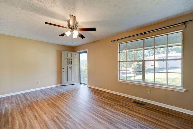 empty room featuring a textured ceiling, light wood-type flooring, visible vents, and baseboards