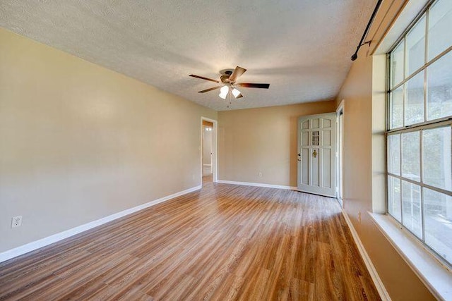 spare room featuring a ceiling fan, light wood-style flooring, baseboards, and a textured ceiling