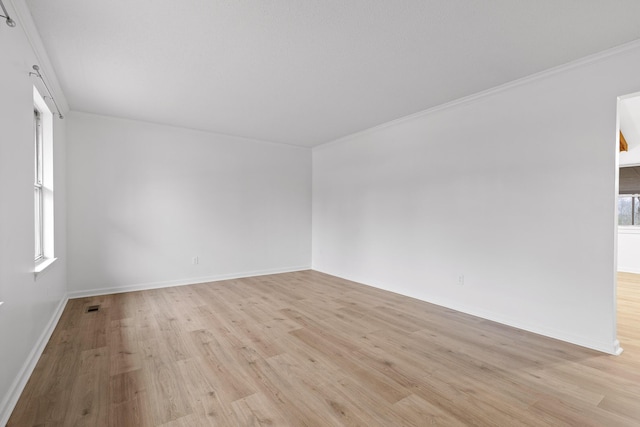 spare room featuring light wood-style floors, visible vents, ornamental molding, and baseboards