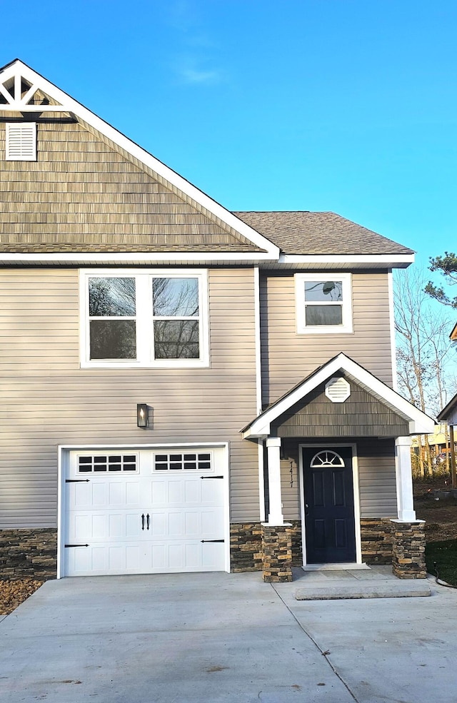 view of front of property featuring a garage, concrete driveway, roof with shingles, and stone siding