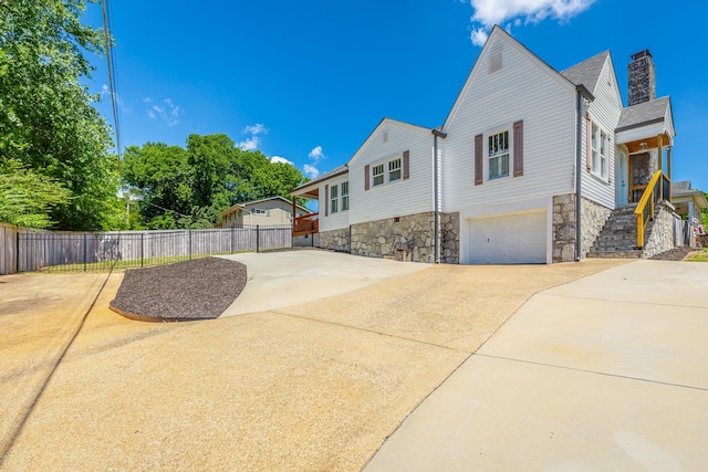 view of side of home featuring a garage, concrete driveway, fence, and a chimney