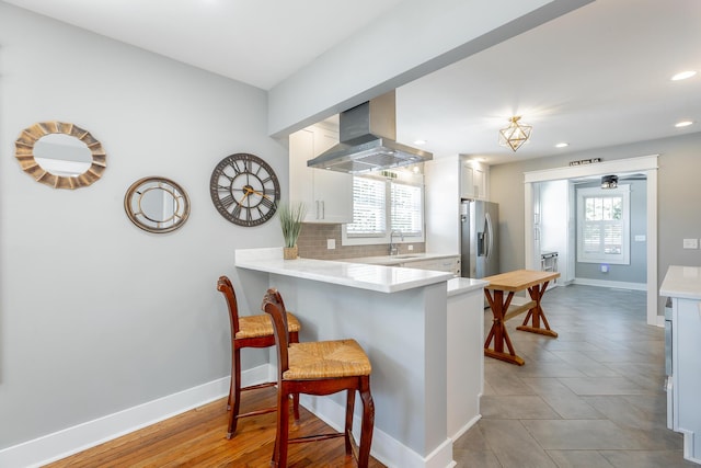 kitchen with light countertops, island range hood, stainless steel fridge, a peninsula, and a kitchen breakfast bar