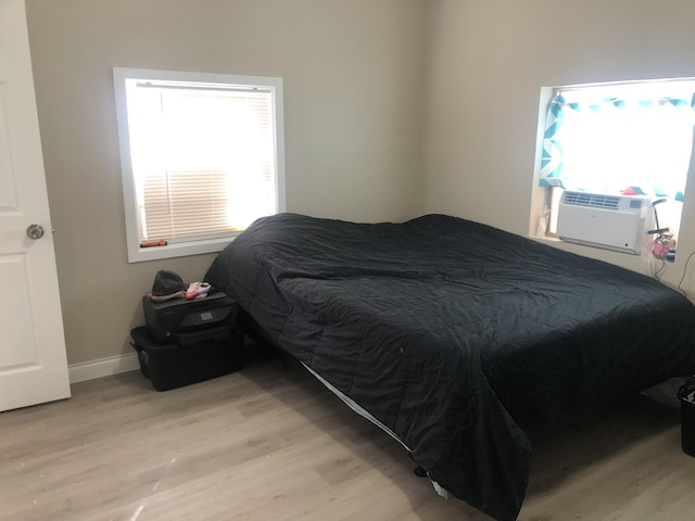 bedroom with cooling unit, multiple windows, light wood-style floors, and baseboards