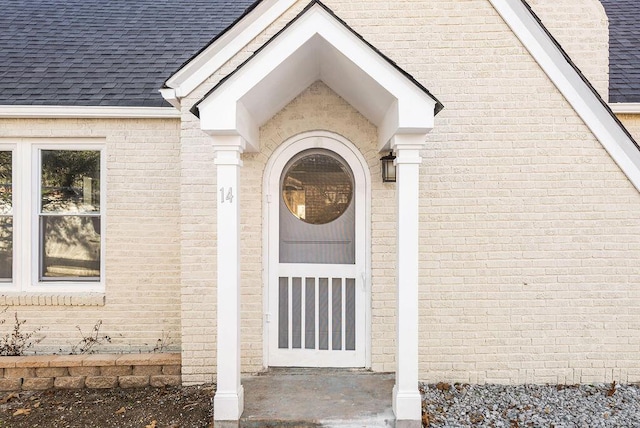 doorway to property with brick siding and a shingled roof