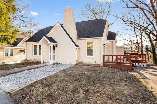 view of front facade featuring a shingled roof, a wooden deck, brick siding, and a chimney