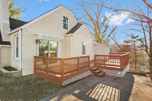 back of property with a deck, a chimney, brick siding, and a shingled roof