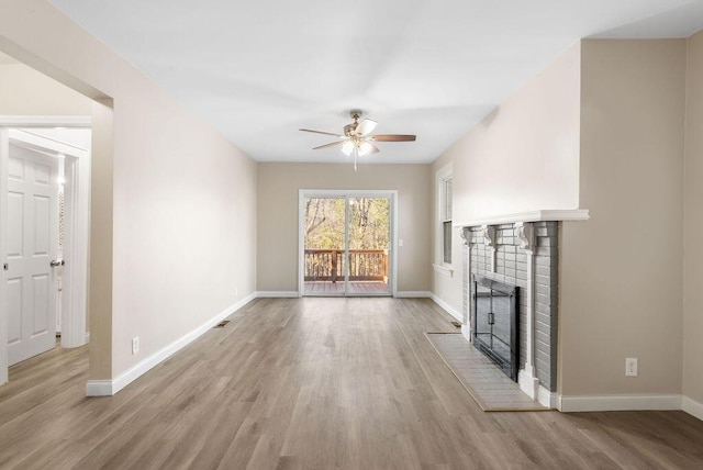 unfurnished living room with a brick fireplace, a ceiling fan, light wood-type flooring, and baseboards