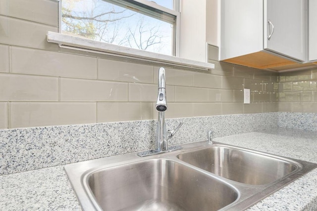 interior details with white cabinetry, light countertops, backsplash, and a sink