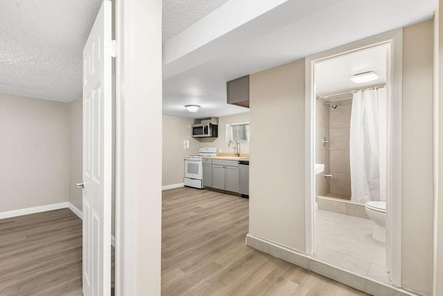 hallway featuring a sink, baseboards, light wood finished floors, and a textured ceiling