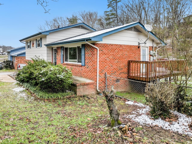 view of side of property featuring a wooden deck, fence, and brick siding