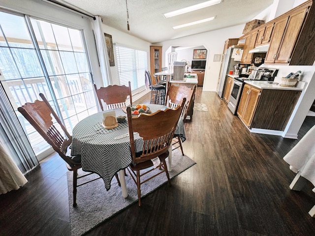 dining room with arched walkways, dark wood-style flooring, vaulted ceiling, and a textured ceiling