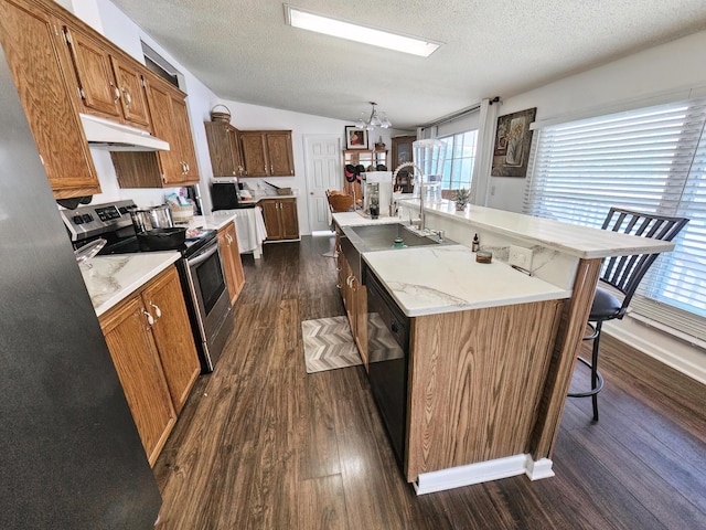 kitchen featuring a breakfast bar area, under cabinet range hood, light countertops, stainless steel range with electric stovetop, and a sink