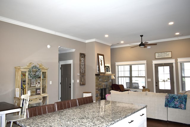 kitchen featuring a stone fireplace, light stone counters, white cabinetry, open floor plan, and ornamental molding