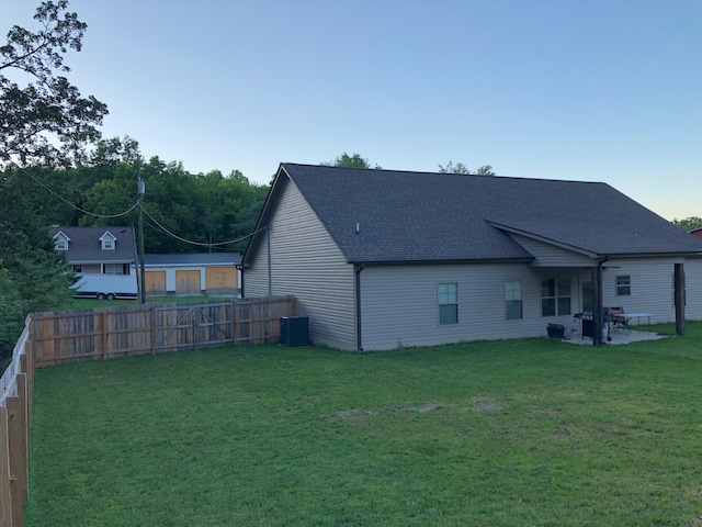 rear view of house featuring roof with shingles, a lawn, central AC unit, a patio area, and a fenced backyard