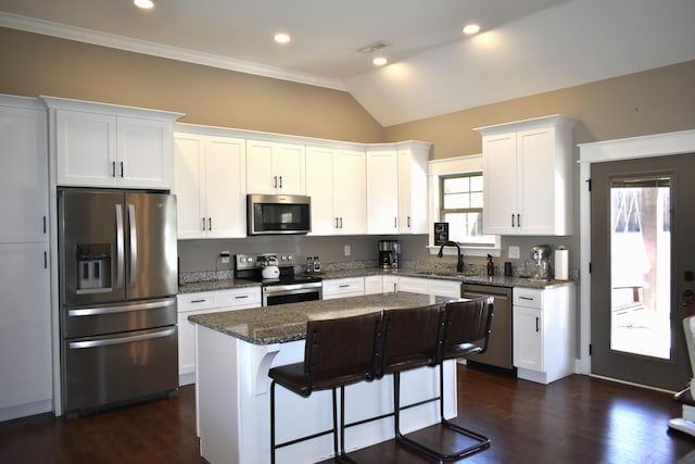 kitchen featuring dark stone counters, a center island, stainless steel appliances, white cabinetry, and a sink