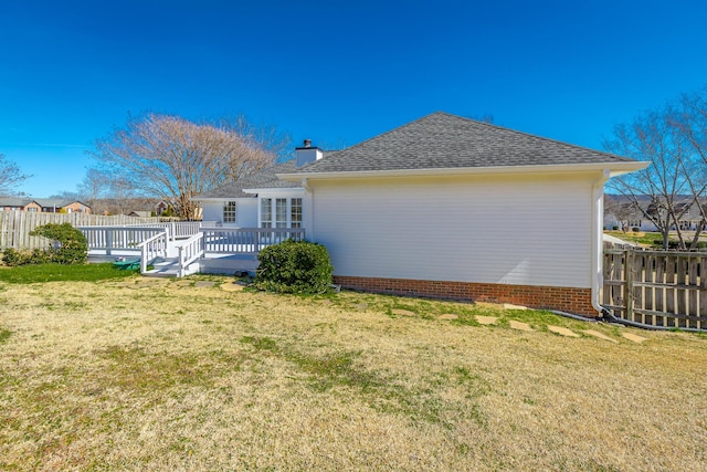 rear view of house featuring a yard, a chimney, a shingled roof, fence, and a deck