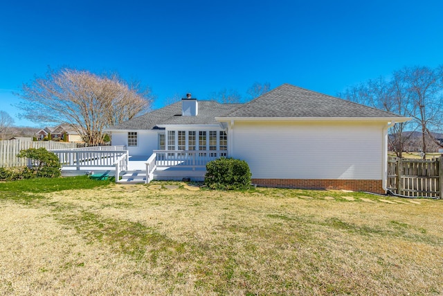 back of house with a deck, a shingled roof, fence, a yard, and a chimney