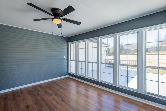 empty room featuring plenty of natural light, dark wood finished floors, and baseboards