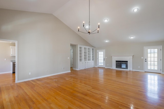 unfurnished living room featuring a chandelier, high vaulted ceiling, light wood-style flooring, baseboards, and a brick fireplace