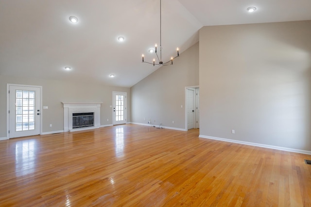 unfurnished living room featuring light wood-type flooring, a brick fireplace, high vaulted ceiling, and an inviting chandelier