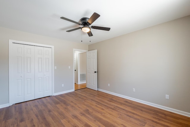 unfurnished bedroom with a closet, visible vents, ceiling fan, wood finished floors, and baseboards