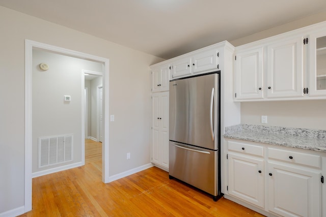 kitchen featuring visible vents, light wood-style floors, freestanding refrigerator, white cabinetry, and baseboards