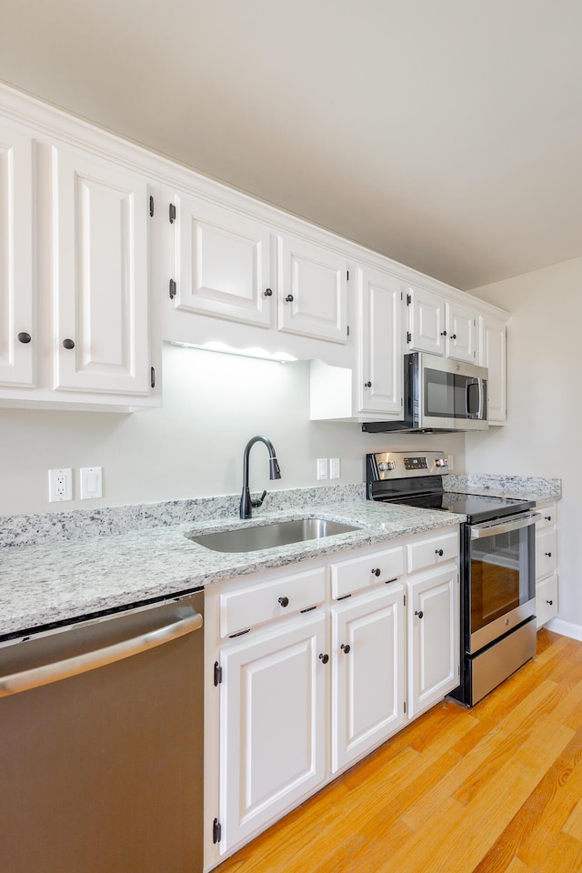 kitchen featuring light stone counters, a sink, white cabinetry, appliances with stainless steel finishes, and light wood finished floors