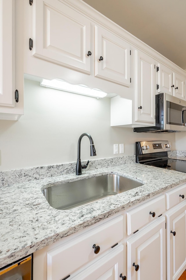 kitchen featuring stainless steel appliances, white cabinets, a sink, and light stone countertops